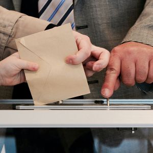 main qui met une enveloppe dans une urne pour voter