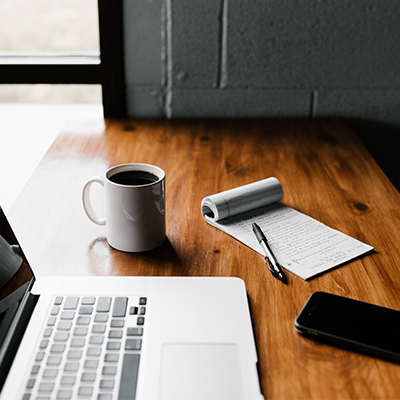 bureau avec un ordinateur, un bloc note et une tasse de café