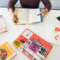 une femme qui lit un livre à côté de son ordinateur