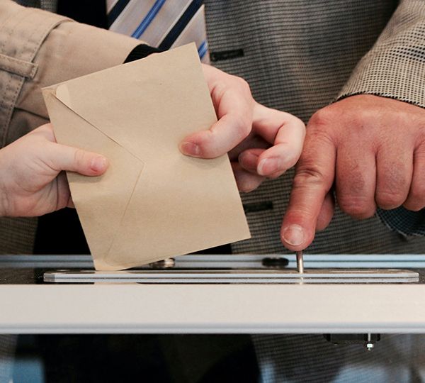 main qui met une enveloppe dans une urne pour voter