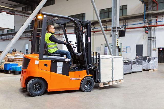 Storehouse employee in uniform working on forklift in modern automatic warehouse. Boxes are on the shelves of the warehouse. Warehousing, machinery concept. Logistics in stock.