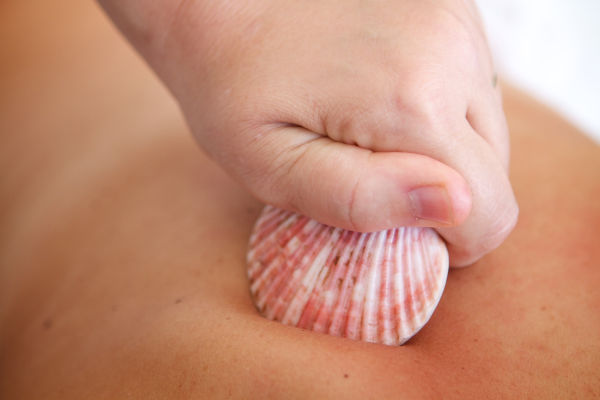 personne qui se fait masser le dos avec un coquillage chaud