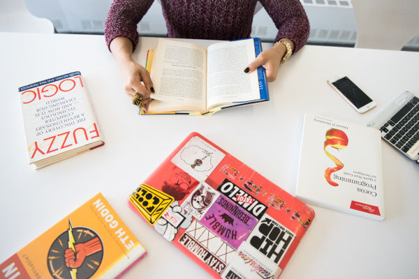 une femme qui lit un livre à côté de son ordinateur