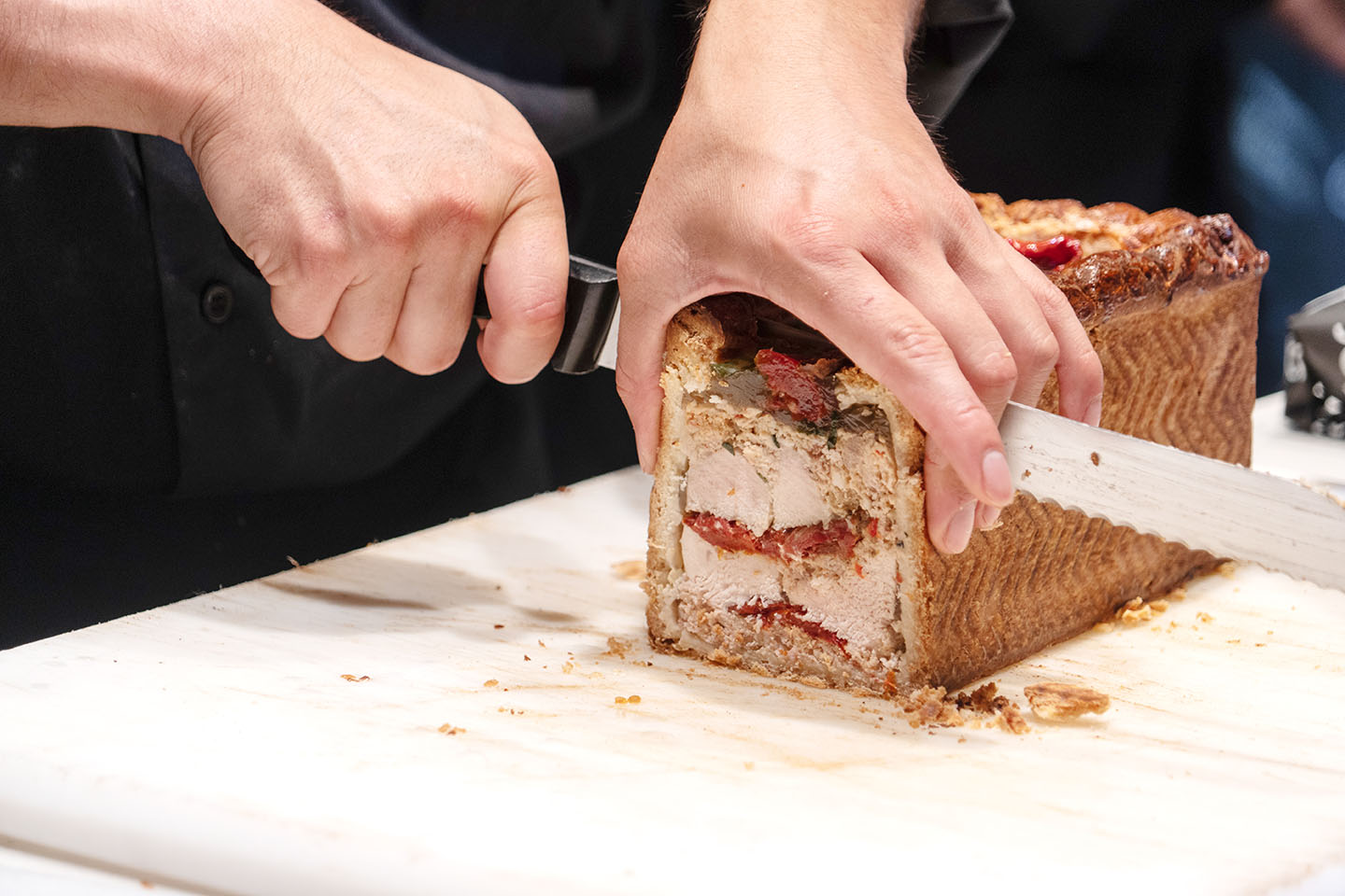 Male hand slicing with a big knife a pate en croute an appetizer