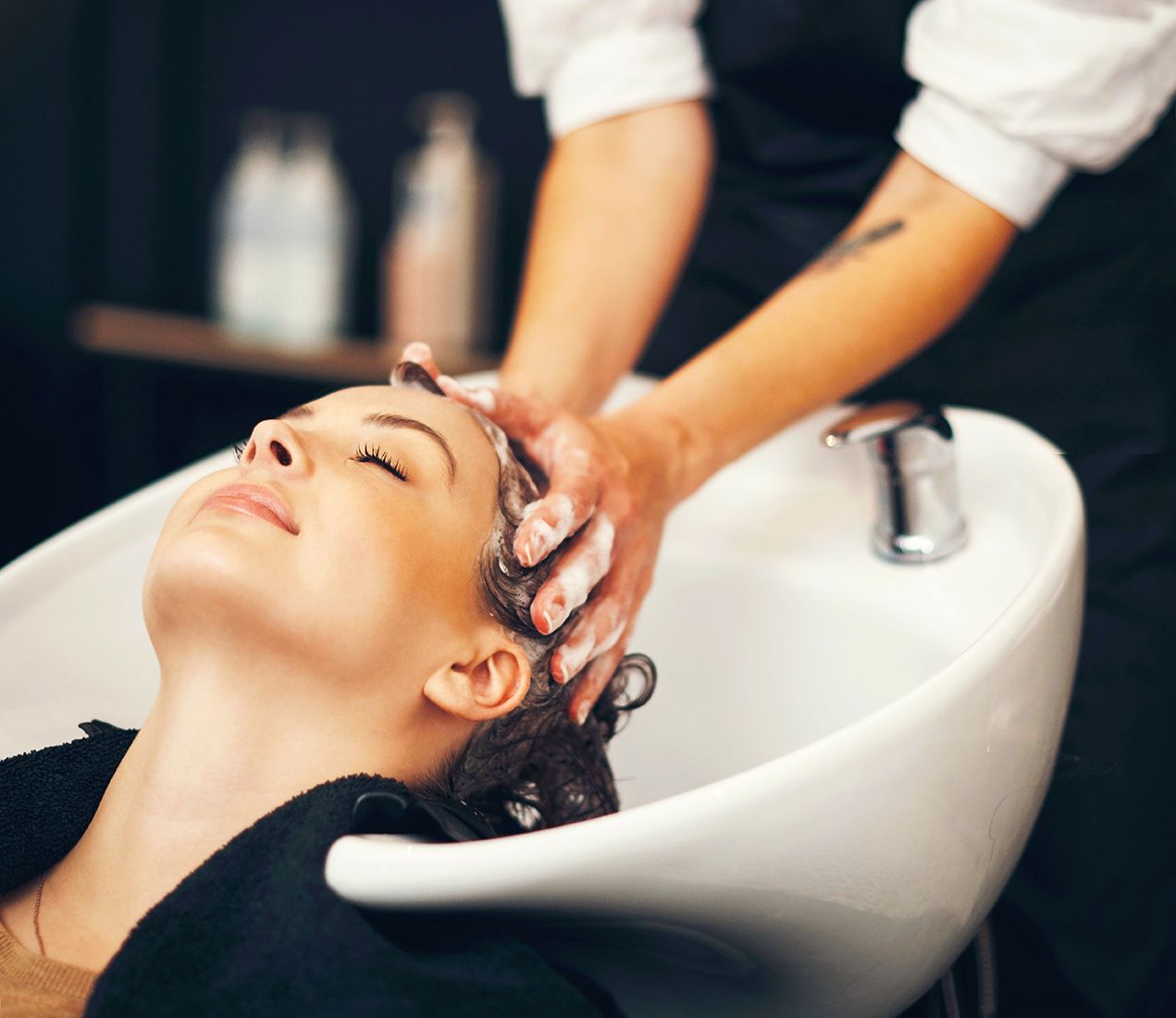 Soap, massage and hairdresser with client in spa, relax and basin for wash and treatment. Hands, salon and hairstyle or balayage dye for happy customer person, keratin or scalp shampoo for hair care.