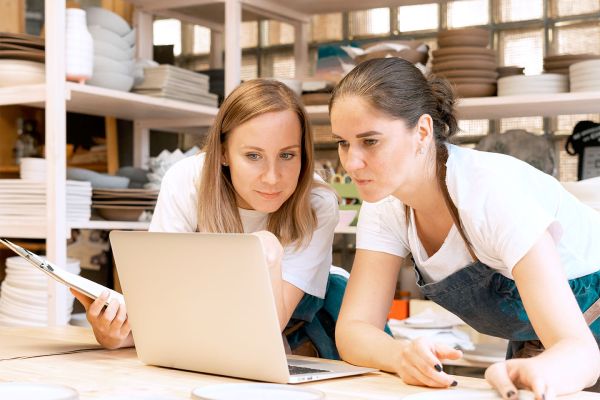 Passer du régime micro au réel : les solutions Two female entrepreneur with laptop in artisan workroom. Waist up portrait of cheerful business woman artisan in pottery studio. Concept for lady in freelance