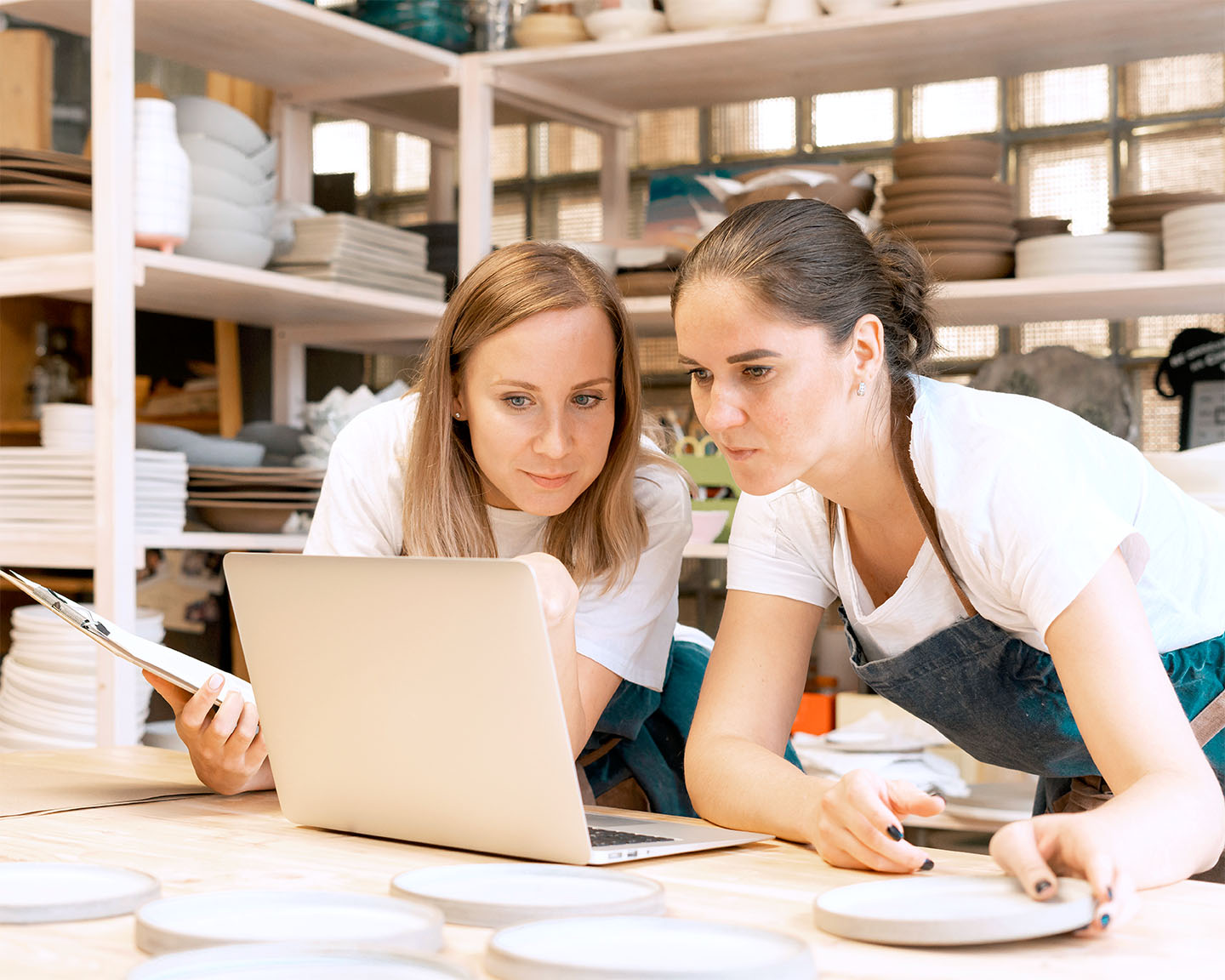 Two female entrepreneur with laptop in artisan workroom. Waist up portrait of cheerful business woman artisan in pottery studio. Concept for lady in freelance