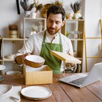 Entrepreneur sells dishes, plates and cups made of clay, ceramics online and packs them in boxes for sending to the delivery service. Small business selling goods on the Internet.